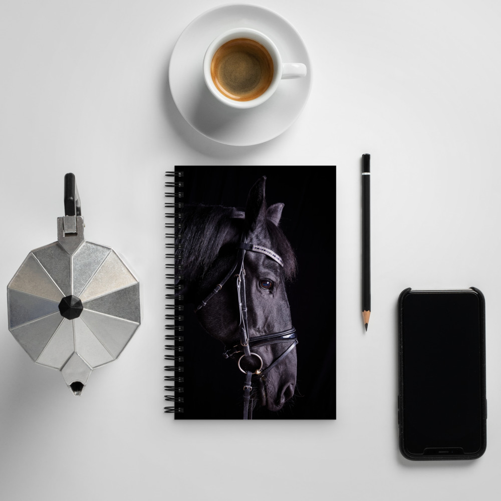 Spiral notebook with a profile of a black horse near a cup of coffee and cell phone