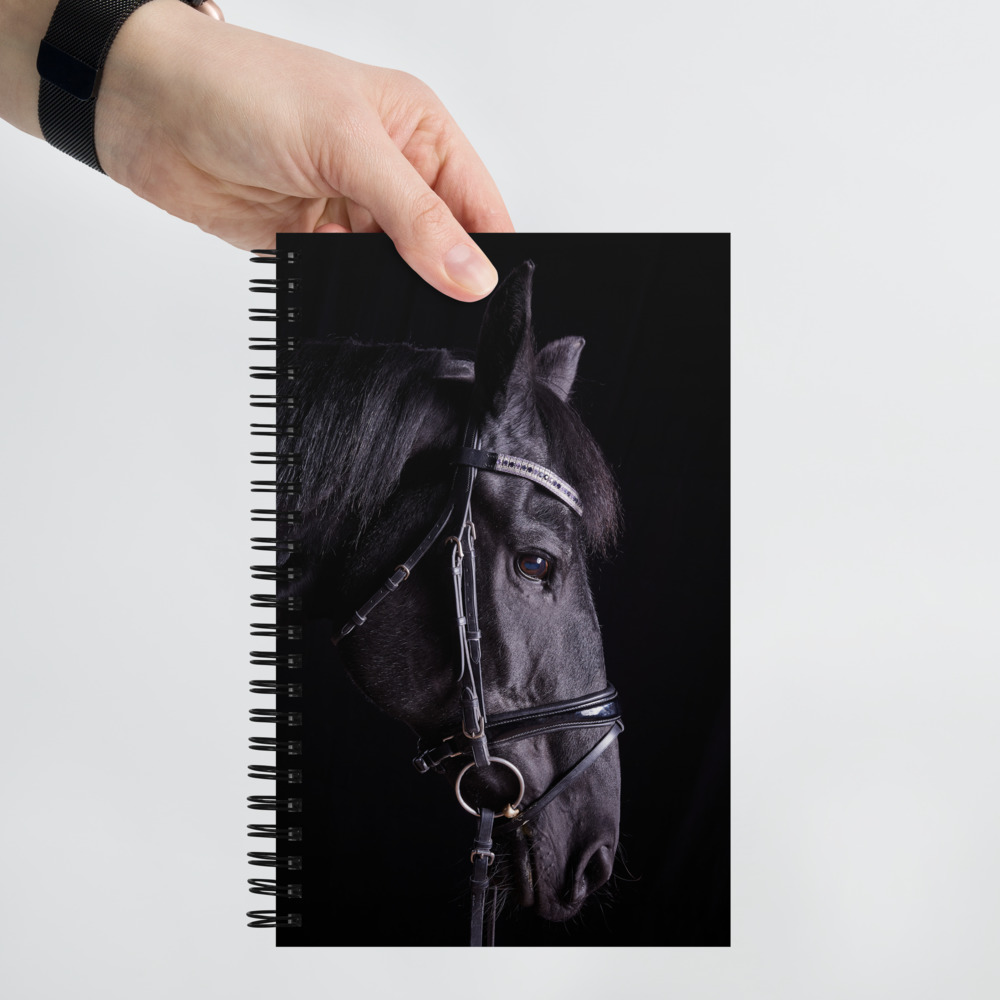 Hand holding a Spiral notebook with a profile of a black horse