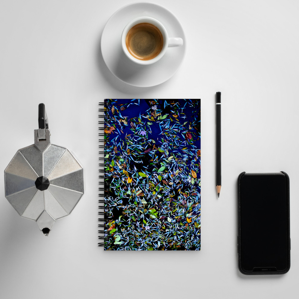 Spiral notebook with a photo of a pond covered with flower petals on its cover next to a coffee cup and cell phone