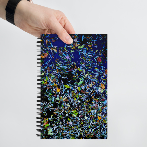 Hand holding a Spiral notebook with a photo of a pond covered with flower petals on its cover