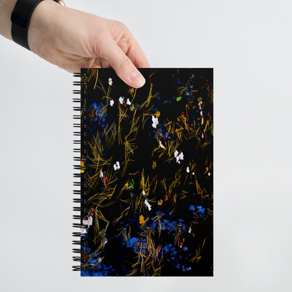 Hand holding a Spiral notebook with a photo of a pond covered with flower petals and leaves on its cover