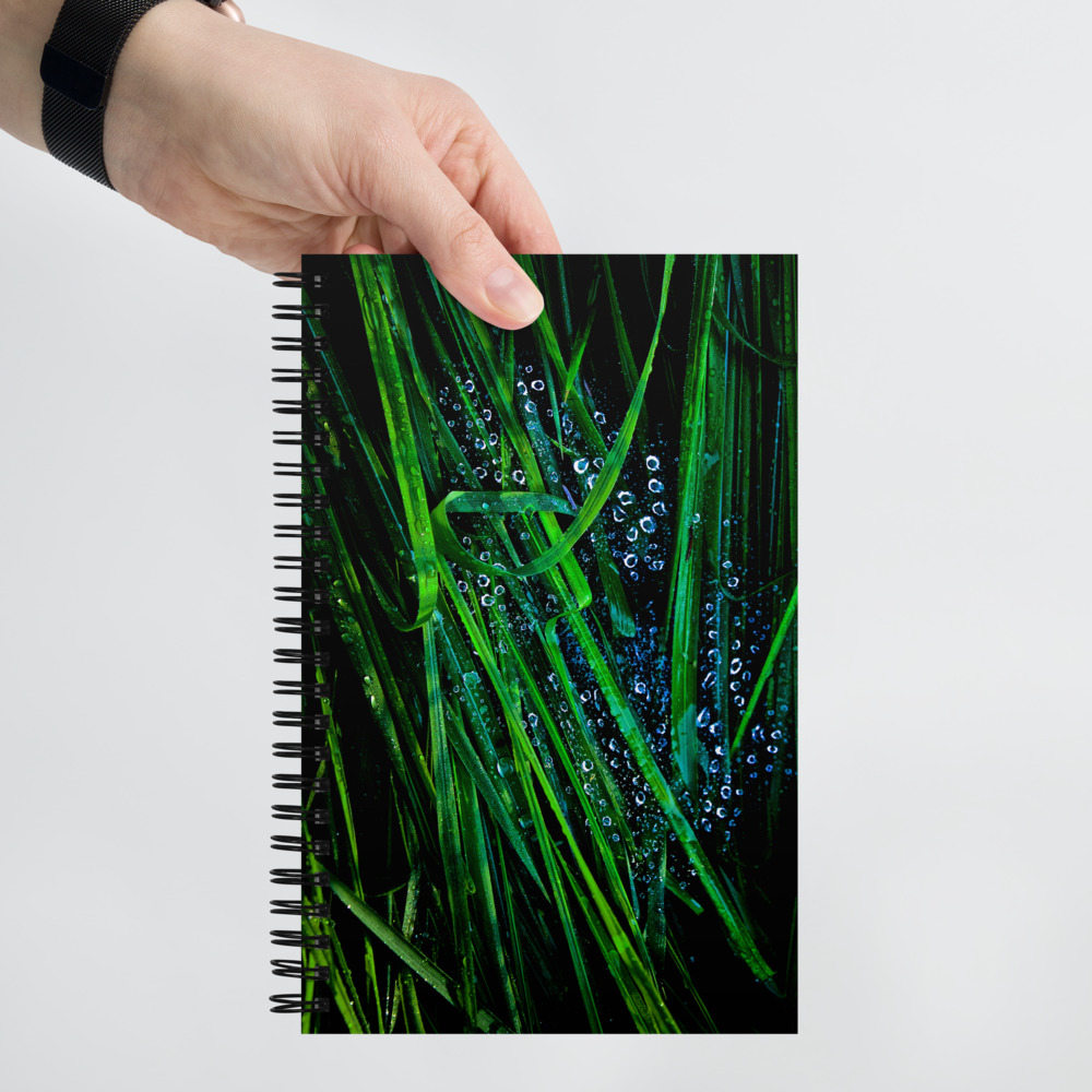 Hand holding a Spiral notebook with a photo of blades of grass covered with water droplets