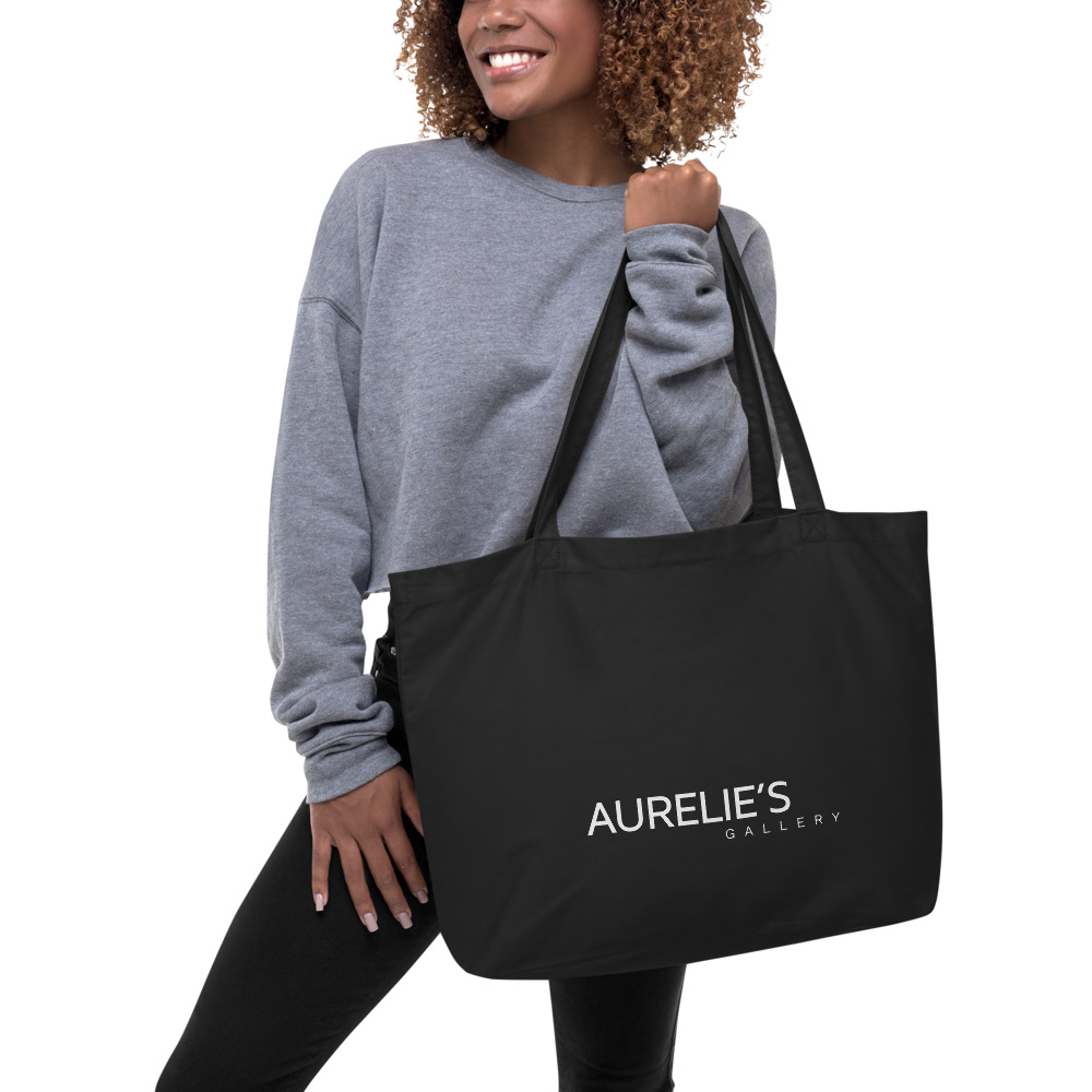 Woman holding a large black tote bag with Aurelie's Gallery written on front side