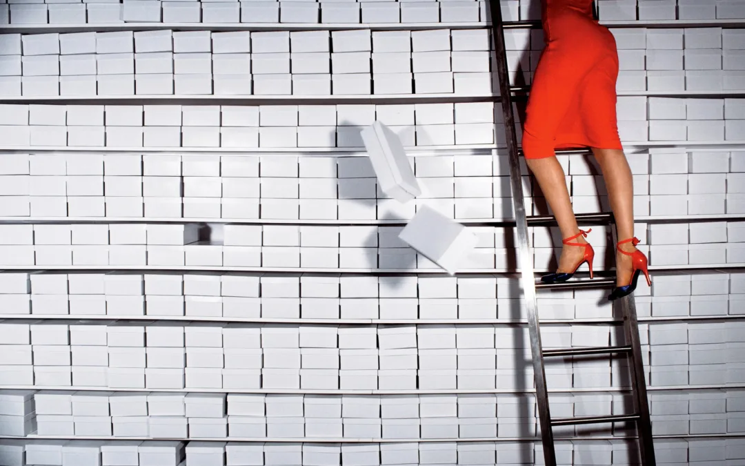 Woman on top of a ladder, leaned against a wall made of show boxes