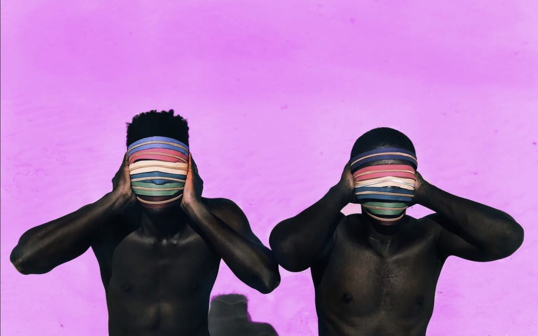 Two shirtless Black men on a beach, facing us, their faces hidden by a scarf