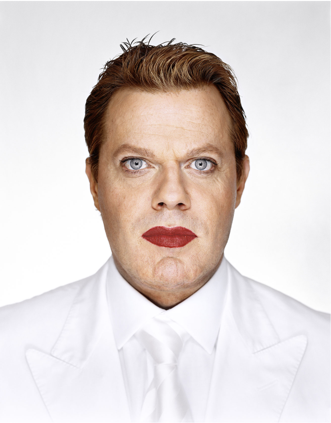 A man in a white suit wearing bright red lipstick
