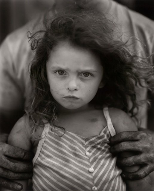 Portrait of a child fiercely looking at us while an adult off camera holds her
