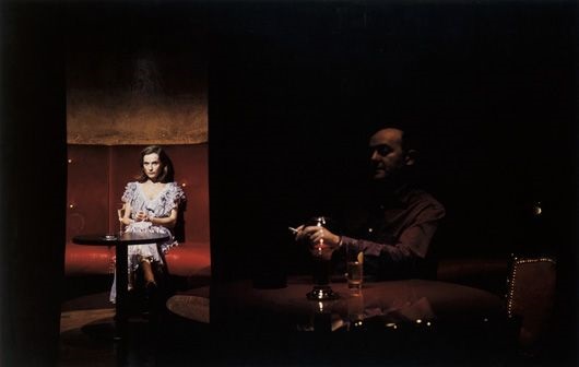 Model sitting in a dark bar, with a man in the foreground, barely visible