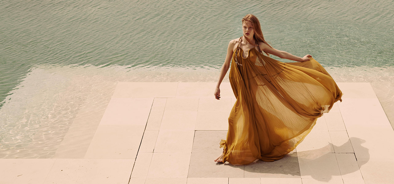 Woman in a flowy dress walking by a swimming pool,