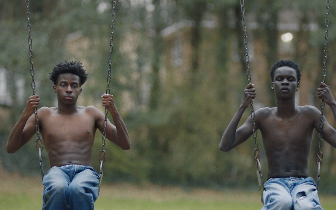 2 young black teens, shirtless, sitting on swings in a park
