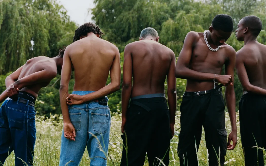 A row of young Black men, standing shirtless in a field