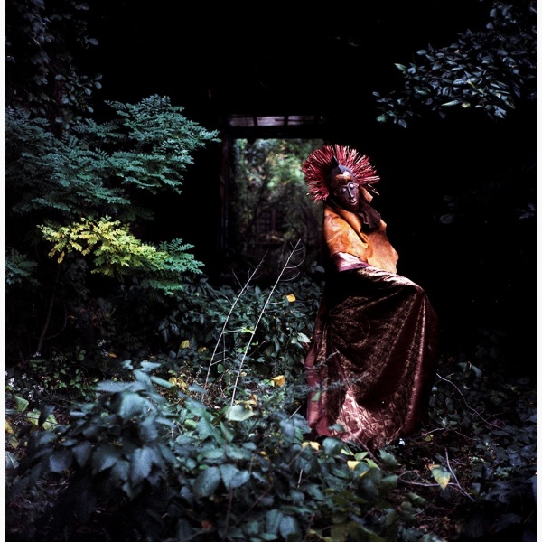 A mysterious figure in an African costume and mask stands in a forest