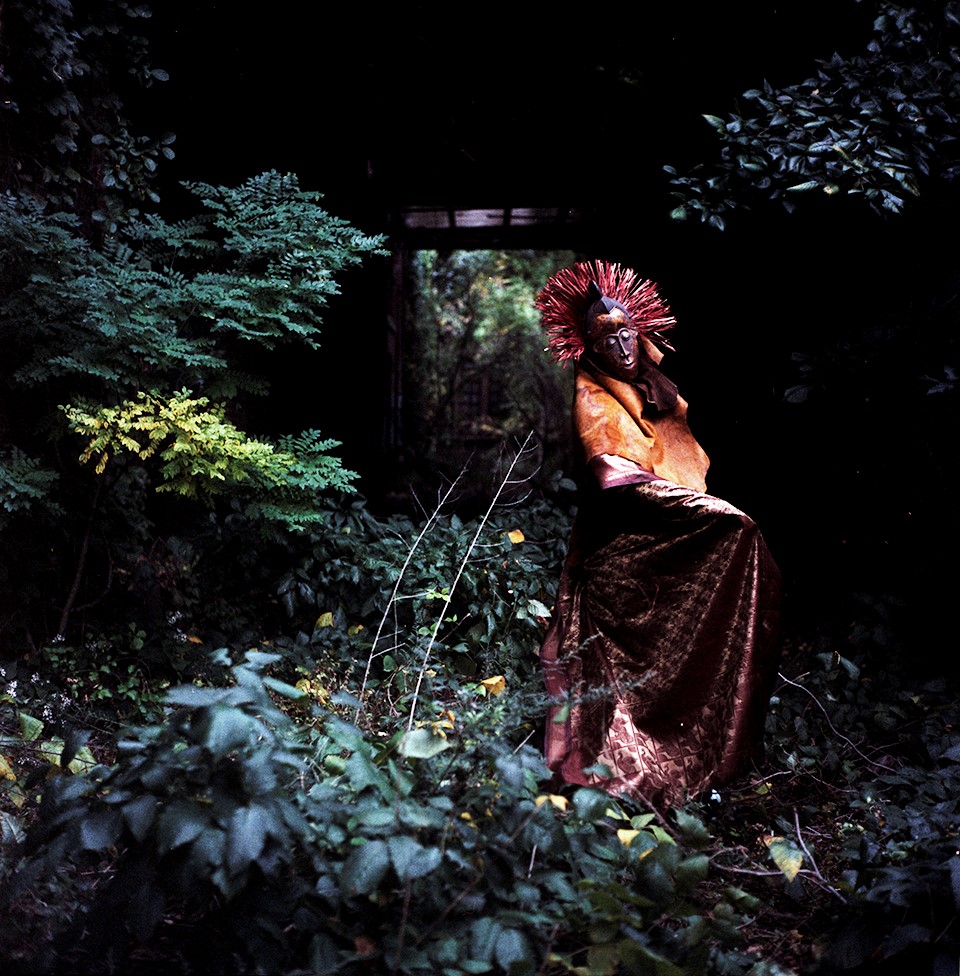 A mysterious figure in an African costume and mask stands in a forest