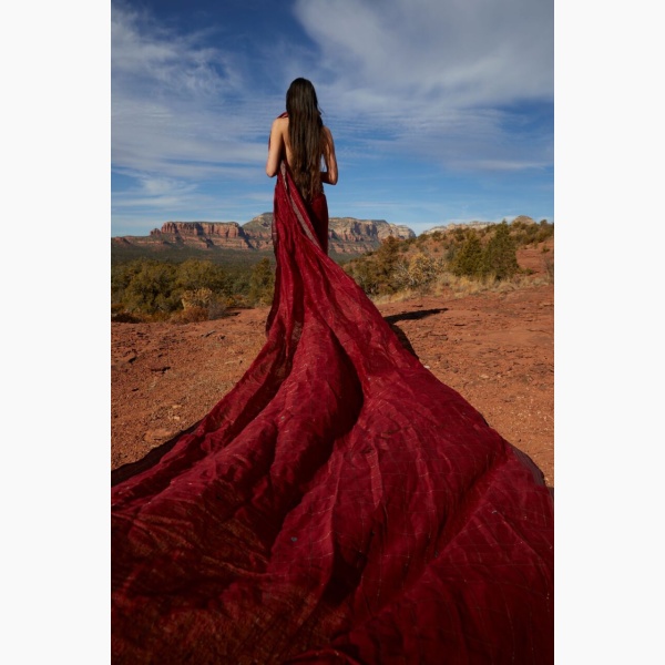 Woman drapped in a long red fabric, standing in a desert