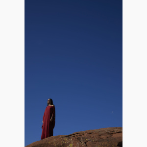 Woman dressed in Indigenous dress, standing on a rock in a desert