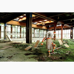 A mysterious figure in an African costume and mask strikes a pose in an abandoned indoor pool