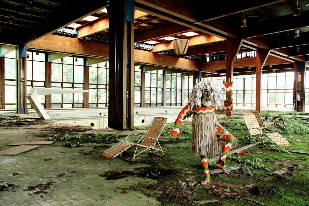 A mysterious figure in an African costume and mask strikes a pose in an abandoned indoor pool
