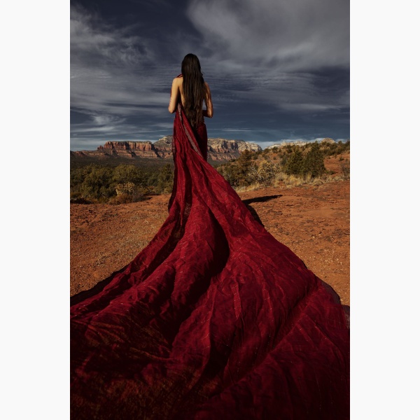 Woman drapped in a long red fabric, standing in a desert