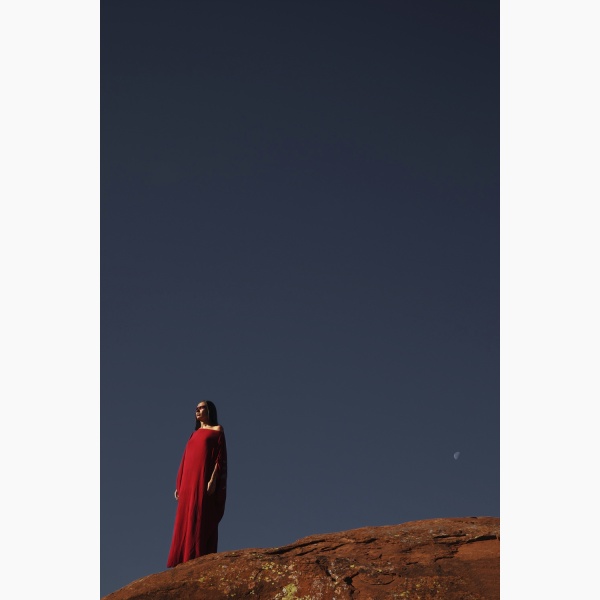 Woman dressed in Indigenous dress, standing on a rock in a desert