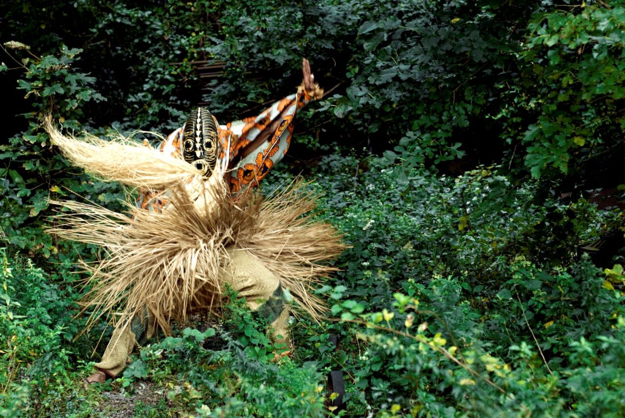 A mysterious figure in a traditional African costume and mask dancing in a forest