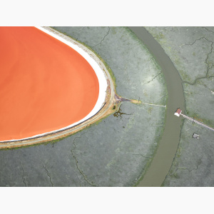 Aerial view of an orange lake, with a small house near it