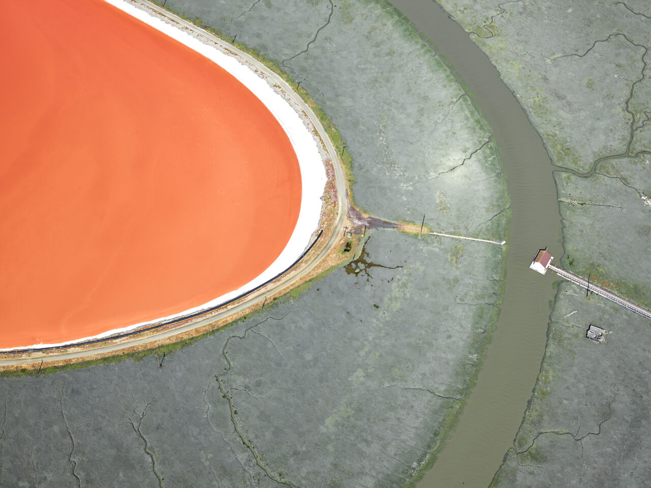 Aerial view of an orange lake, with a small house near it