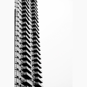 Silouhette of a skyscraper against the sky, with a lone person on their balcony