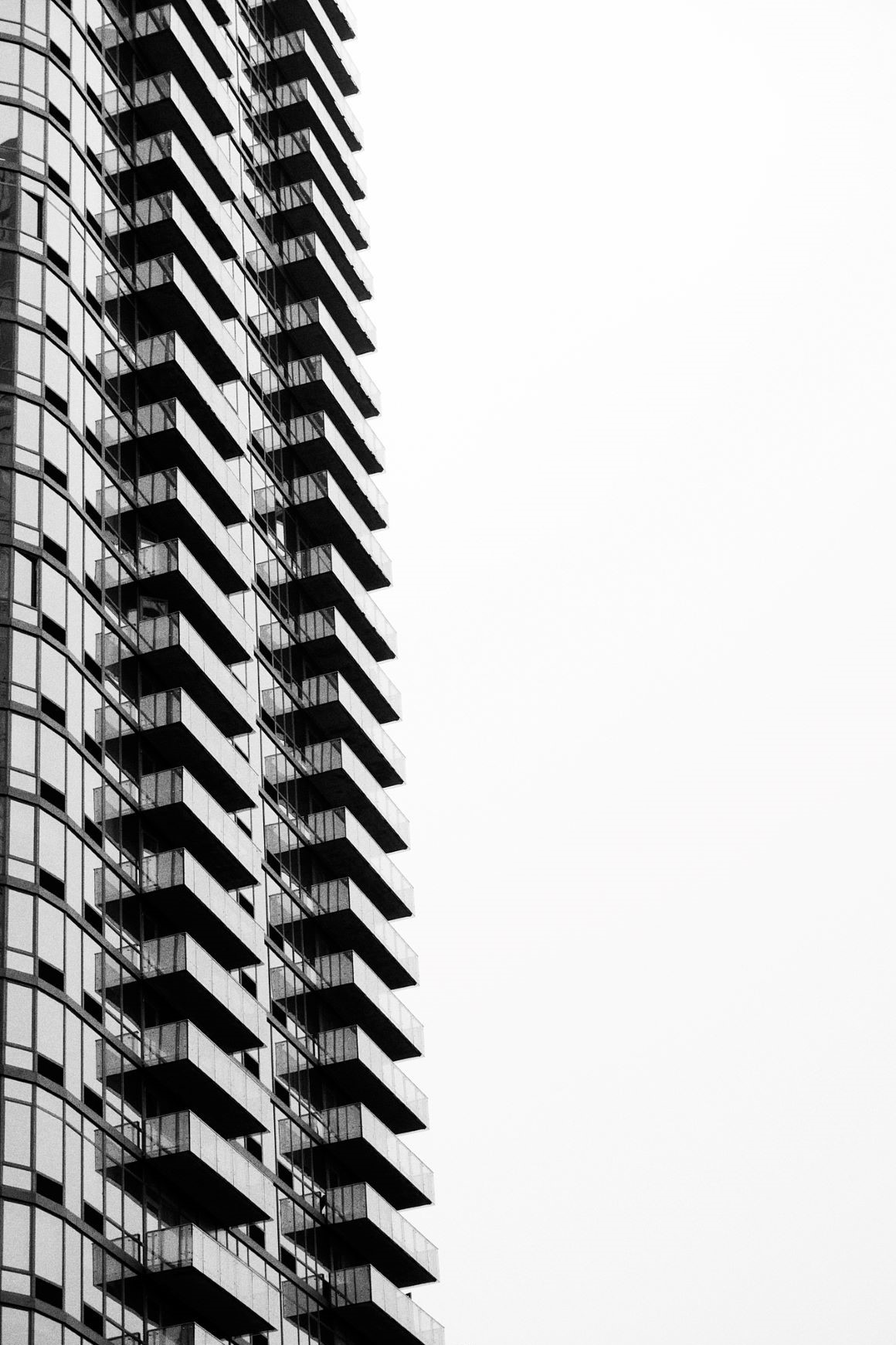 Silouhette of a skyscraper against the sky, with a lone person on their balcony