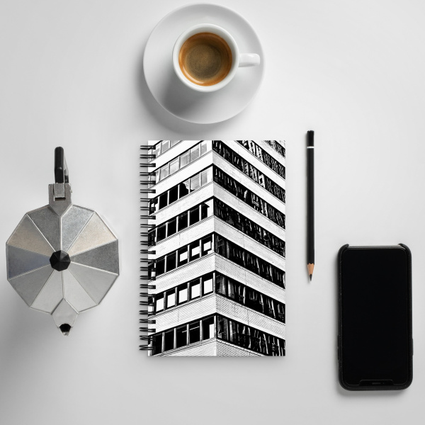 Laying on a table, next to a coffee cup, Notebook with a photograph of a skyscraper façade