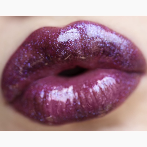 Close-up of a woman's mouth making a kiss shape and wearing glossy lipstick