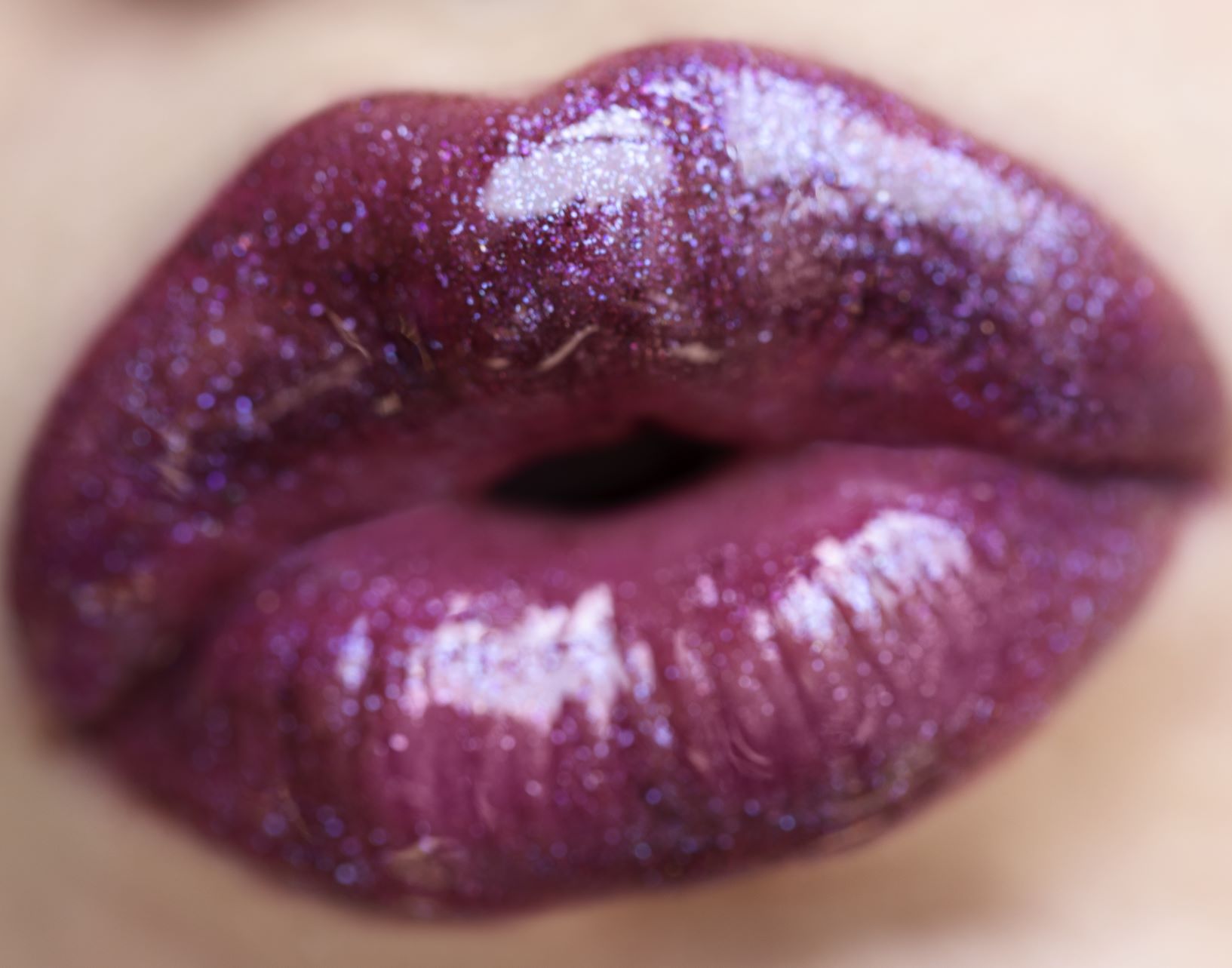 Close-up of a woman's mouth making a kiss shape and wearing glossy lipstick