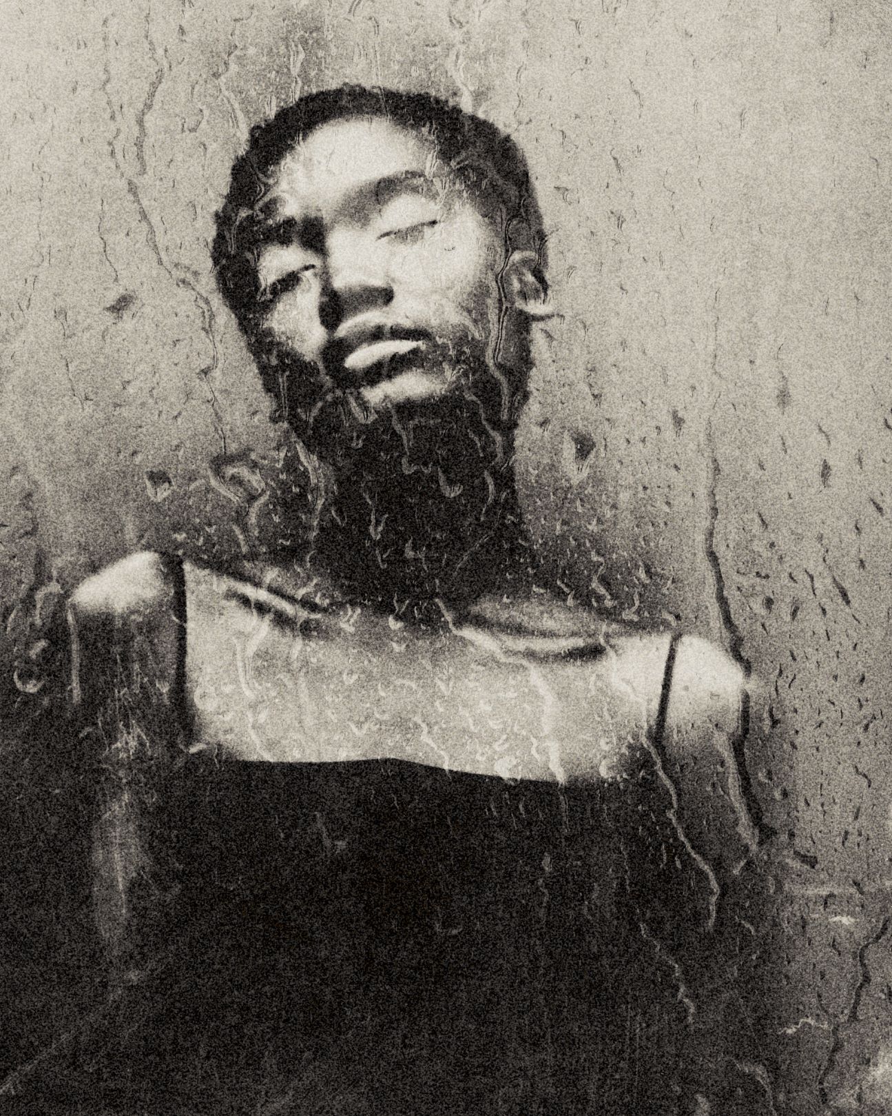 Young Black woman with her eyes closed, standing by a wall, as seen through a rainy window pane