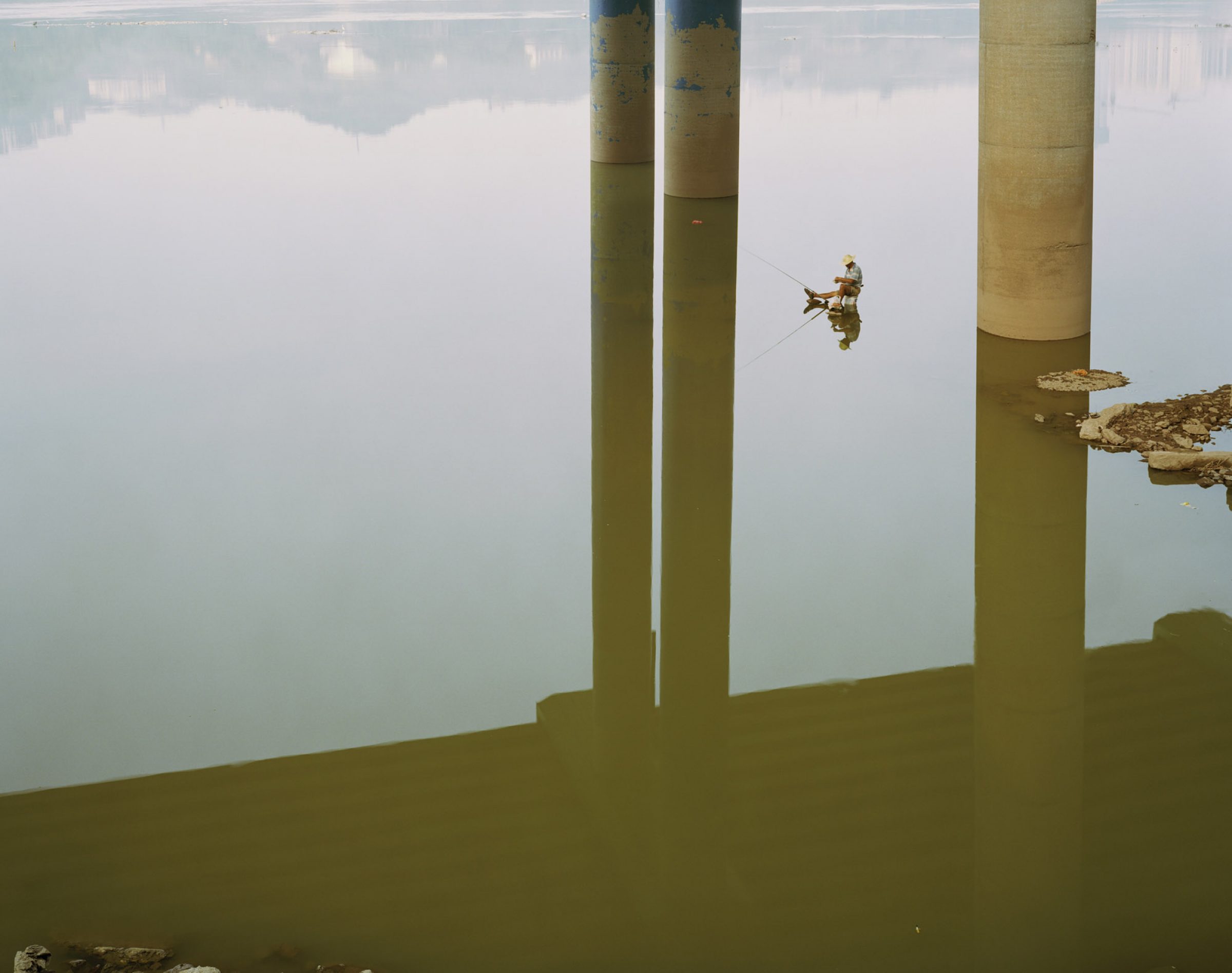 Lone man on a small boat in a river, under a gigantic overpass