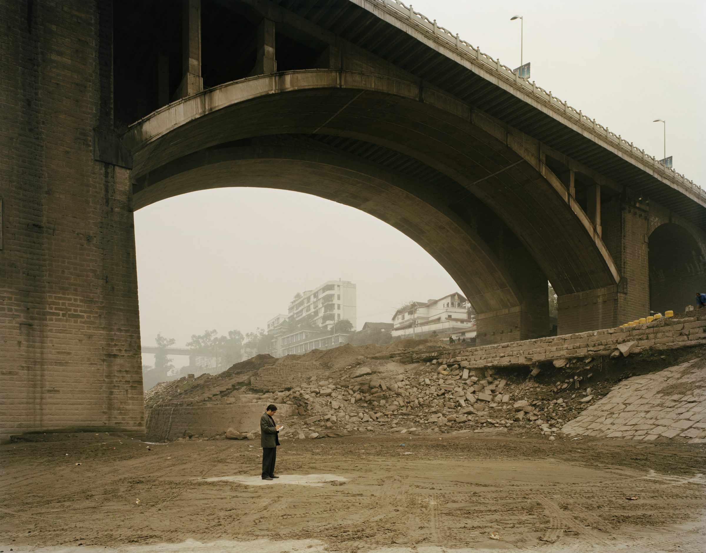 A man, standing alone under a large bridge