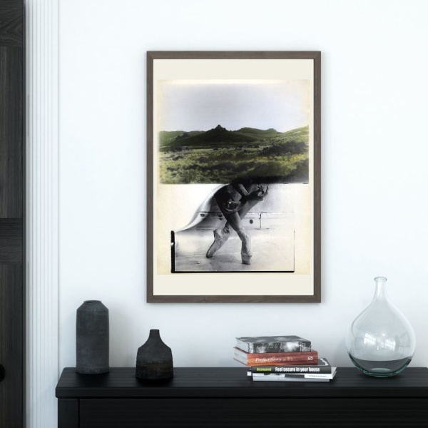 Framed print of a collage print showing a hilly landscape and a dancer on pointed feet, hanging above a console table