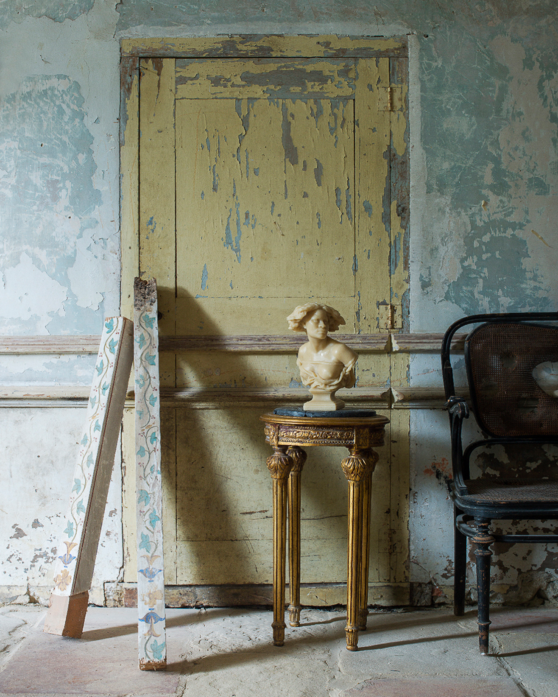 A rom with a few decorative elements - an ornate bench, a marble bust sitting on a table, some painted wood panels