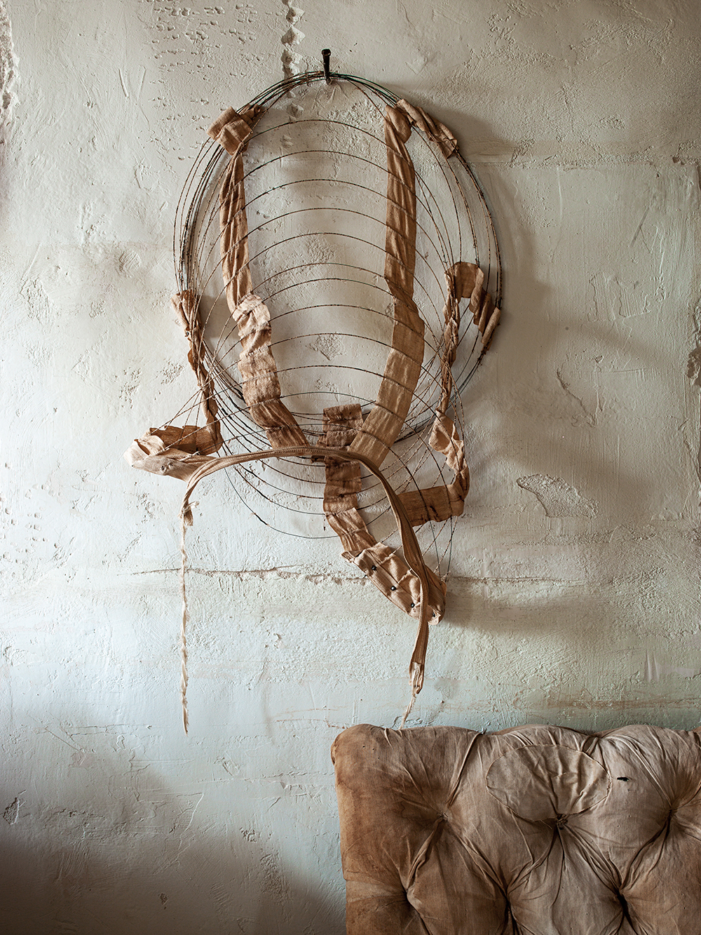 The metal remant of a 19th-century hooped skirt hangs against a plastered wall, with a couch under it