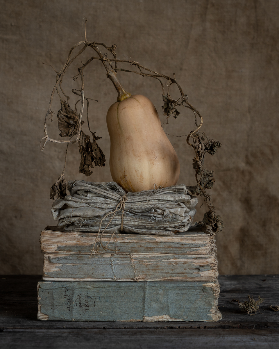 A pumpkin sits in top of folded napkins and old books on a table