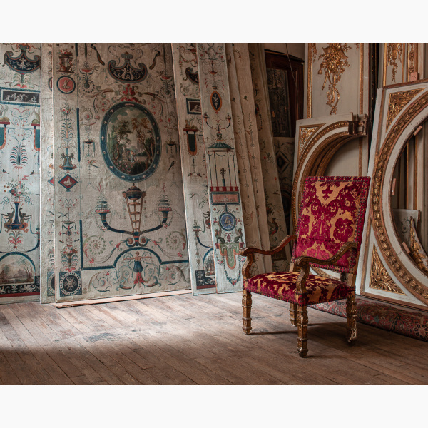 An ornate antique armchair sits in a room filled with painted decors