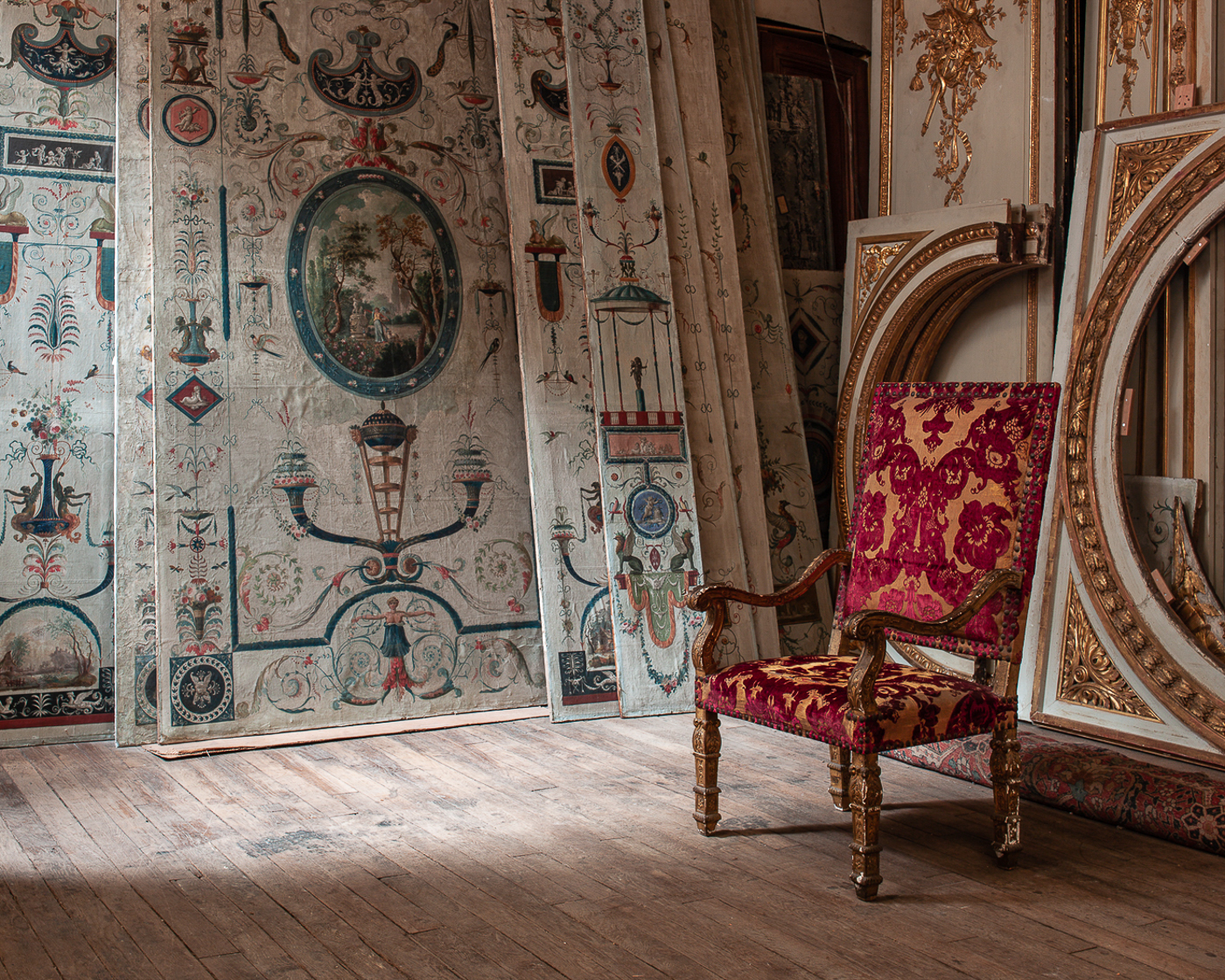 An ornate antique armchair sits in a room filled with painted decors