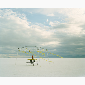 A metal structure covered with Caution Tape stands in the middle of a salt flat against a stormy sky