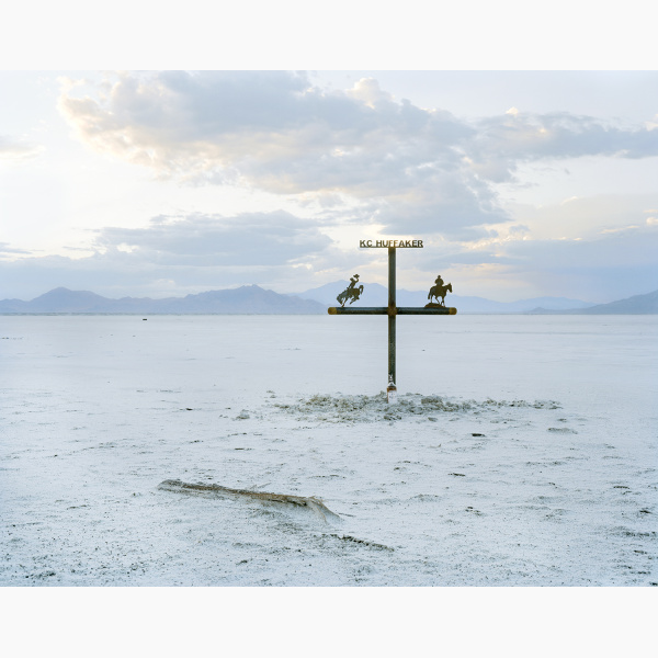 A metal cross stands in the middle of salt flat at dusk with mountains in the far distance