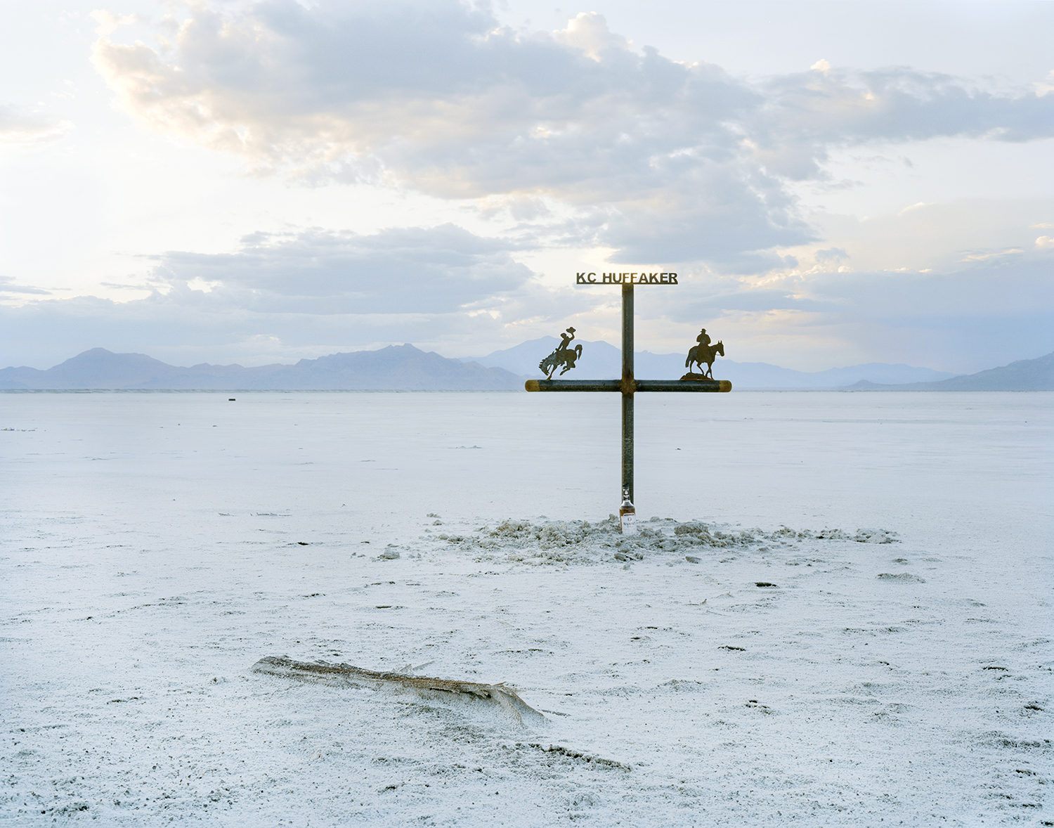 A metal cross stands in the middle of salt flat at dusk with mountains in the far distance