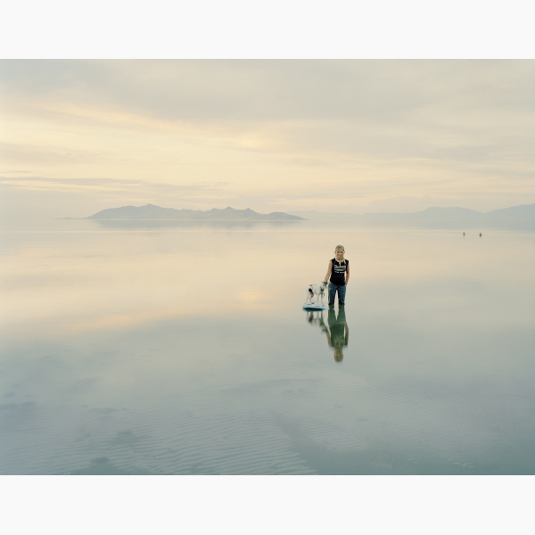 A little girl stands with her dog in a pool of water on a salt flat