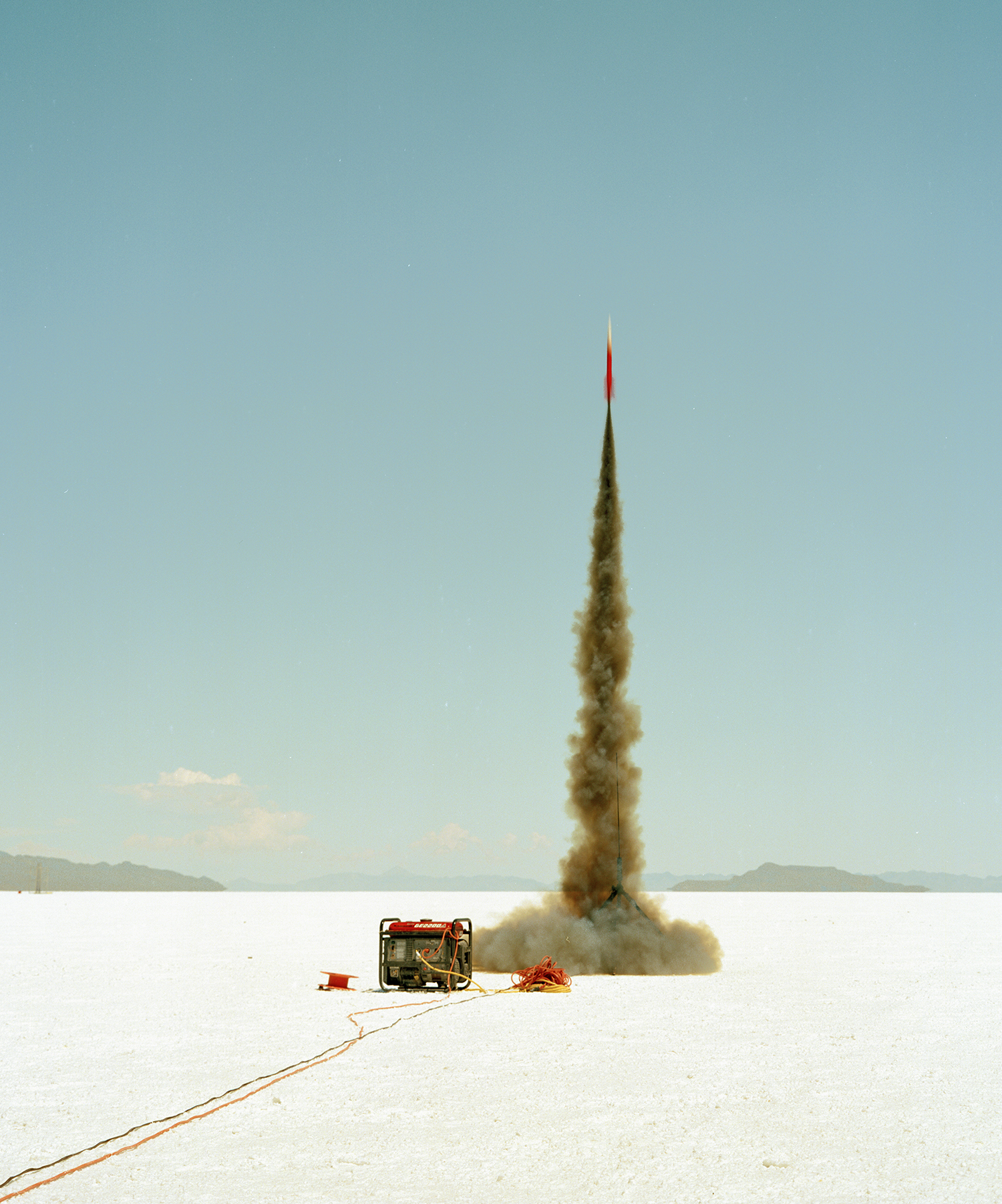 A small rocket launches into air, with a generator nearby, on a salt flat