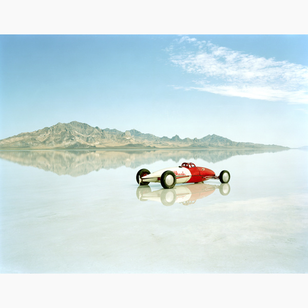 A lone racing car stands in a salt flat with mountains in the distance