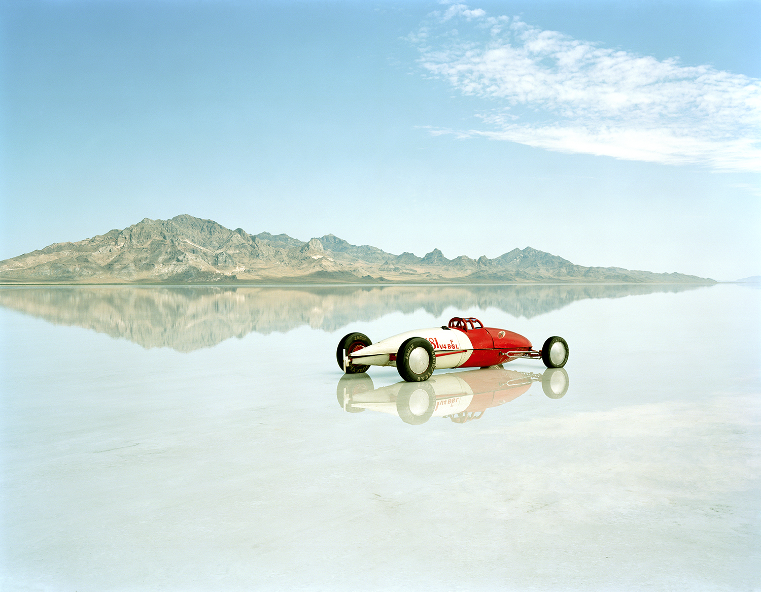 A lone racing car stands in a salt flat with mountains in the distance