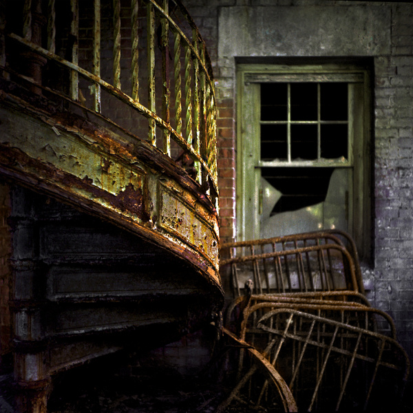 A broken glass door and a spiral rusty metal staircase stand in an abandoned building