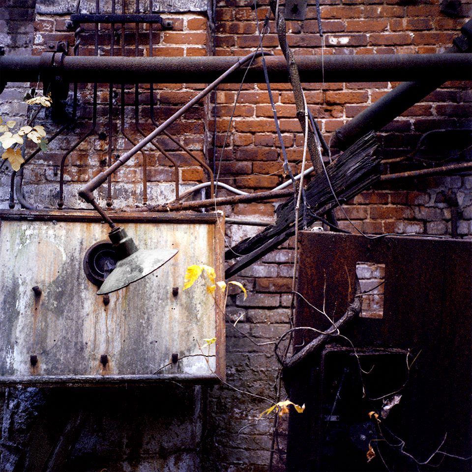 A broken lamp hangs above a rusty metal box attached to a crumbling wall